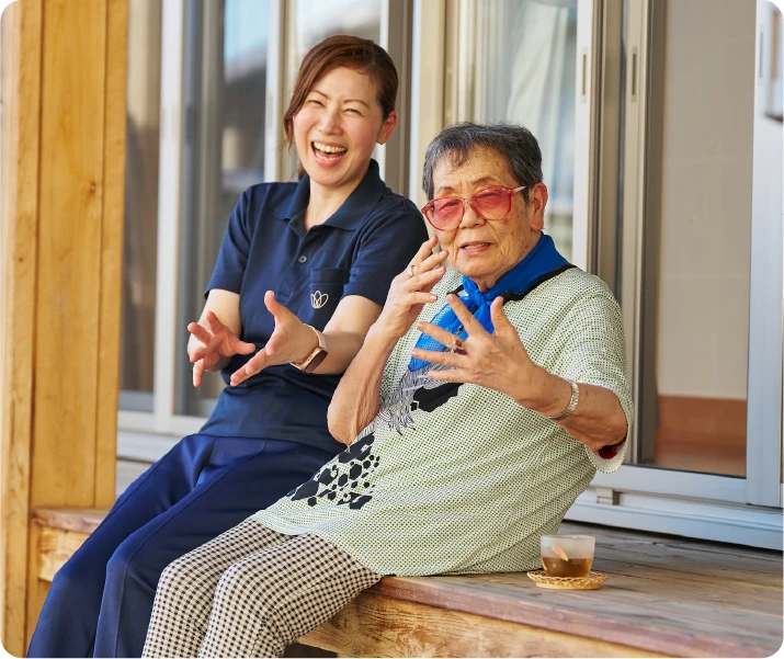 縁側でお茶をしながらカメラに向けてポーズをとる中瀬千春さんと仲田富枝さん